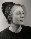 Hattmode visas på varuhuset  Nordiska Kompaniet i Stockholm 1936.
En ung kvinna poserar i halvprofil iförd en liten hatt av präglat skinn, möjligen krokodil. Hatten har ett litet, finmaskigt flor.