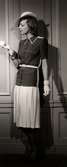 Dammode, kvinnlig modell poserar iklädd veckad kjol, kortärmad dräktjacka med skärp, hanskar och liten hatt. Nordiska Kompaniet 1938.