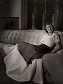 Franska avdelningen vid Nordiska Kompaniet 1941. En kvinnlig modell sitter i en soffa iförd kortätmad överdel och lång vid kjol med breda horisontala fält.
