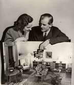 Brud och hem utställningen på varuhuset Nordiska Kompaniet i Stockholm 1944. Man och kvinna med modell av en möblerad lägenhet.