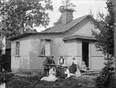 Sommarnöje i skärgården. Några kvinnor sitter framför en mindre sommarvilla. 
