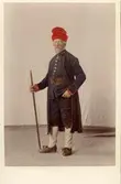 Man i helfigur klädd i kyrkdräkt från Järvsö socken, Hälsingland. Handkolorerat fotografi. 