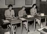 Modellerna visar passande klädesplagg för kontoristen, februari 1952. Tre kvinnor skriver på maskin. Nordiska Kompaniet.