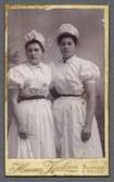 Två unga kvinnor i likartade vita dräkter. Kabinettkort.