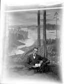 Porträtt, angett som sjävporträtt  av Georg Renström, sittande framför en uppspikad fotofond föreställande ett landskap med utsikt. Samma fotofond finns på flera av fotografens bilder. Se rubriken Referenser, relaterade objekt.