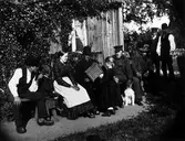 Personer på bänk. Ägaren till Oktorpsgården Åke Lundqvist med hund, brodern Erik som spelar dragspel, en piga och en dräng samt ett okänt barn. Flickan som står framför är Hanna, dottern på gården. 