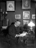 Dr Julius Levenhagen vid bordet med en bok. Fotogenlampa.
