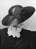 Kvinnlig modell i hatt från Maria Guy. Stråhatt med dekorband. Tygros vid halsen. Nordiska Kompaniet, Stockholm.