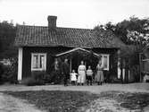 Kvinnor, barn och man framför torp, före 1933