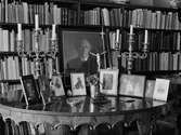 Bostadsinteriör med inramade fotografier på bord. Flera av dem avbildar ärkebiskop Nathan Söderblom. Uppsala 1948