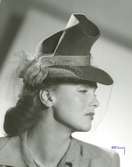 Porträtt av kvinna i hatt med flor och hattband.