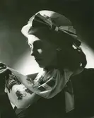 Porträtt av kvinna i hatt med rosett på sidan, samt örhängen och scarf.