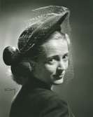 Porträtt av kvinna med hatt i svart filt med fjäderbollar och flor. Hatt använd vid franska avdelningens uppvisning september 1947.
