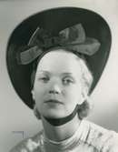 Fb, Porträtt av kvinna i hatt av Madame Alphonsine. Svart filt med hakband.