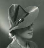 Fb, Porträtt av kvinna i hatt av Rose Descat. Brun filt med mockagarnityr.