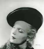Fb, Porträtt av kvinna i hatt av Elsa Schiaparelli. Den nya silkesflätan saturne, underbrätte av svart sammet.