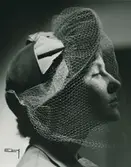 Porträtt av kvinna i mossgrön velourhatt med guldfärgat grasgrainband och flor. Modell från Maison Claude Saint Cyr.