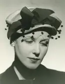 Porträtt av kvinna i guldfärgad stråhatt med svart ripsband.