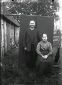 Johanna Andersdotter och Alexander Andreasson, Höghult, Drängsered. Bilden är tagen utomhus. Man har hängt ett stycke tyg över en stör som bakgrund för fotograferingen. Till vänster i bild syns en ekonomibyggnad.