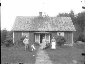 Gruppbild. Familje- eller släktbild? Liten mangårdsbyggnad.