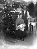 Familjebild av Jenny och Karl Johansson med babyn Ivar, fotograferade inomhus framför en julgran.  Galtabo, Drängsered. Ivar Karlsson var född 1914-12-09. Modern Jenny var antingen född Löwhult eller bodde på gården Löwhult. Möjligen kan Jenny och Karl hetat Johannesson.