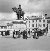 En grupp kvinnor och män samlade kring dubbelstatyn från 1915 på Kungstorget i Uddevalla