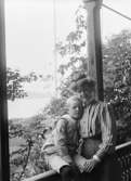 En pojke sitter på ett verandaräcke, bredvid honom står en kvinna med armen om pojken, Villa Klippan, Gustavsberg