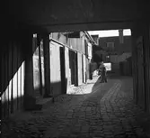 Port in till gårdsplan vid Smedjegatan 38 i Jönköping. En arbetsklädd man med en sopkvast i handen står inne på den gatstensbelagda gårdsplanen.