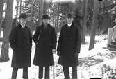 Lungkliniken, Eksjö. Tre män i överrock, Gustav Andersson i mitten med käpp, i bakgrunden barrskog samt en trappa med träräcke.