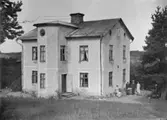 Enköping, Familjen Herkes hus, sett från nordost. De två äldre på bilden är sannolikt paret Herke. Paret flyttade dit 1897. Huset revs i och med att nuvarande tre hyreshus byggdes 1941.