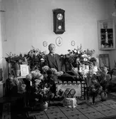 En man firar sin 50-årsdag. Han sitter i soffan omgiven av blommor och gratulationskort.