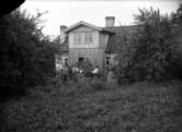 Grupp framför bostadshus, oidentifierad, ev. 29 juni 1901