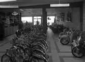 Bild från Stig Malms Sport- och cykelaffär på Vättergatan i Huskvarna i samband med öppnandet den 25 april 1955. Husqvarnafabrikens produkter, såsom cyklar, mopeder och motorcyklar, var välrepresenterade. På bilden syns även en scooter från Husqvarna.