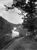 År 1907. Vattenfallet i Huskvarna vid Ebbes bruk med Munksjö kraftstation. Två män och två kvinnor tar en paus på promenaden vid gångvägen som sträcker sig utmed kanten.