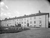 Bostadshus på Mellangatan 6-8 i Jönköping år 1936. På gården finns en sandlåda och 18 barn sitter på gräsmattan bredvid.