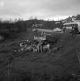 En drickabil från Krönleins bryggeri har parkerats lite för nära sluttningen utmed Ådalsvägen på Jutaholm den 5 december 1960. Marken ger vika och den förarlösa bilen rasar ner och hamnar på taket. Läskedrycker och öl far åt alla håll.