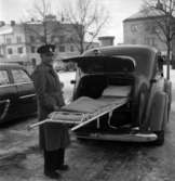 Taxichaufför Arvid Stenlund kunde även använda sin bil som ambulans. För att få in båren fick han fälla sätena. Denna bil, en Volvo-sugga, ska ha varit i bruk ända in på 1960-talet. Bilden är tagen utanför taxistationen med varuhuset Unionen i bakgrunden.