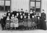 Pojkar och flickor som står framför en husvägg vid Ranntorps småskola. Fröken Anna Svedberg med skolklass. Förkryssad elev är Anna Hasselberg (gift Larsson), född 1895.