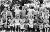 Gruppfoto med flickor och pojkar utomhus, vid Gamla Fässbergsskolan. Magister Daniel Nilsson med elever i 5:e klass. 

Fässbergsskolan låg i sydvästra Solängen och var en av Mölndals tre äldsta skolor, byggd i början av 1860-talet. Byggnaden brändes ned 1971.