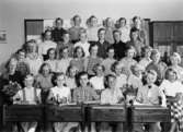 Flickor och pojkar stående i klassrum på Kvarnbyskolan i Mölndal år 1952. De två främsta raderna sitter i bänkar. Med på fotot är givaren Margit Hellström (f. Willumsen).