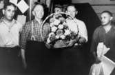 Anders Eliasson, ordförande i Pappers (pappersarbetarnas fackförbund) 63:an, med tre andra män. Eliasson håller en blomstergrupp i famnen.