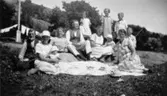 Sommarklädda kvinnor, män och barn som har kaffekalas utomhus. Hallen i Kållered 1929-1950-tal.