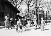 Bosgårdens barnträdgård 1938-1945. Förskollärare och barn som leker utomhus vid en klätterställning.