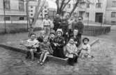 Några barn som står i en sandlåda uppställda för fotografering. Okänd plats 1945-.