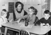 Bosgårdens barnträdgård 1938-1945. Lärare och barn som sitter och pysslar vid ett bord.