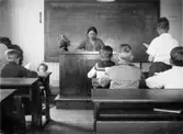 Valdeborg Johansson med sina elever i klassrummet, våren 1934. Text på fotots baksida: 