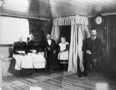 Interiörbild från Lilla Vommedal, 1900-tal. Från vänster sitter Maria Eriksson, Anna Carlson (piga hos Maria), Anton, flickan Ulla som står vid sparlakanssängen samt Karl.