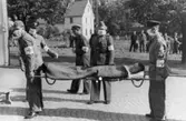 Flykting från koncentrationsläger förs till karantänsförläggningen i Kvarnbyskolan 1945. Röda korsets personal bär den sjuke på bår. I bakgrunden ses Frälsningsarméns byggnad på Kvarnbygatan 19 (idag: Kvarnbygatan 6).