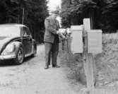 Bilkåkande lantbrevbäraren Cyril Falk på linjen Lönsboda-Hunshult-Björkhult-Lönsboda. Vid brevlådesamling i Hunshult, Blekingegränsen. Foton maj 1961.
