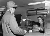 Interiör från postkontoret Kallhäll, 1960.  Kassadisken med kund och
kassörska.